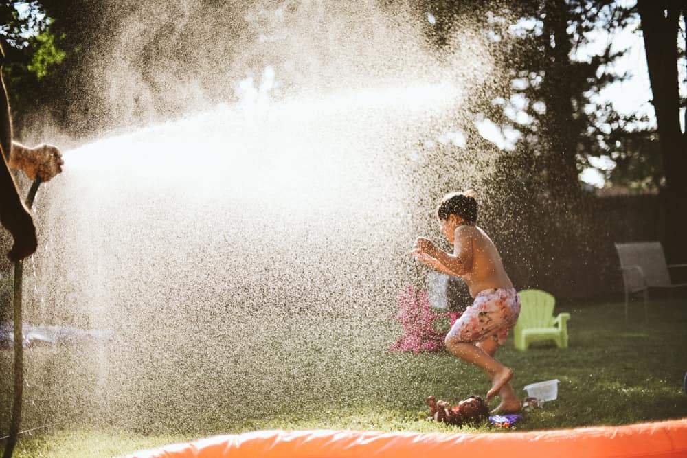 A boy playing in a sprinkler in a sunny backyard