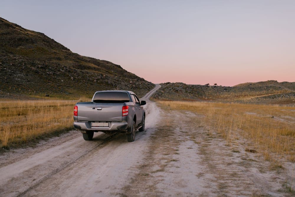 A pickup truck on a dusty rural road at sunset