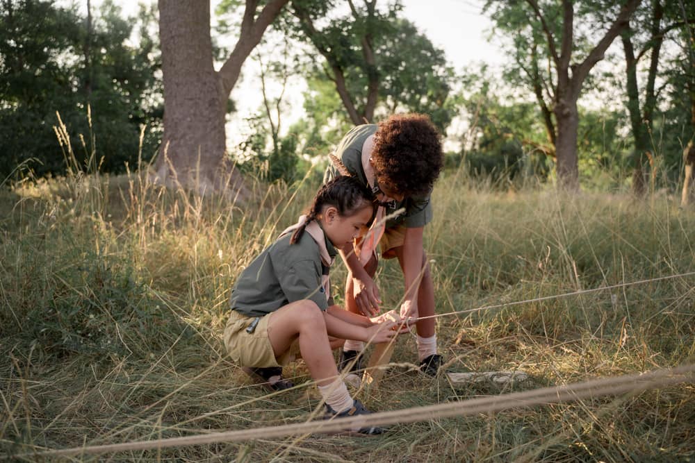Two young scouts tying knots at a grassy campsite