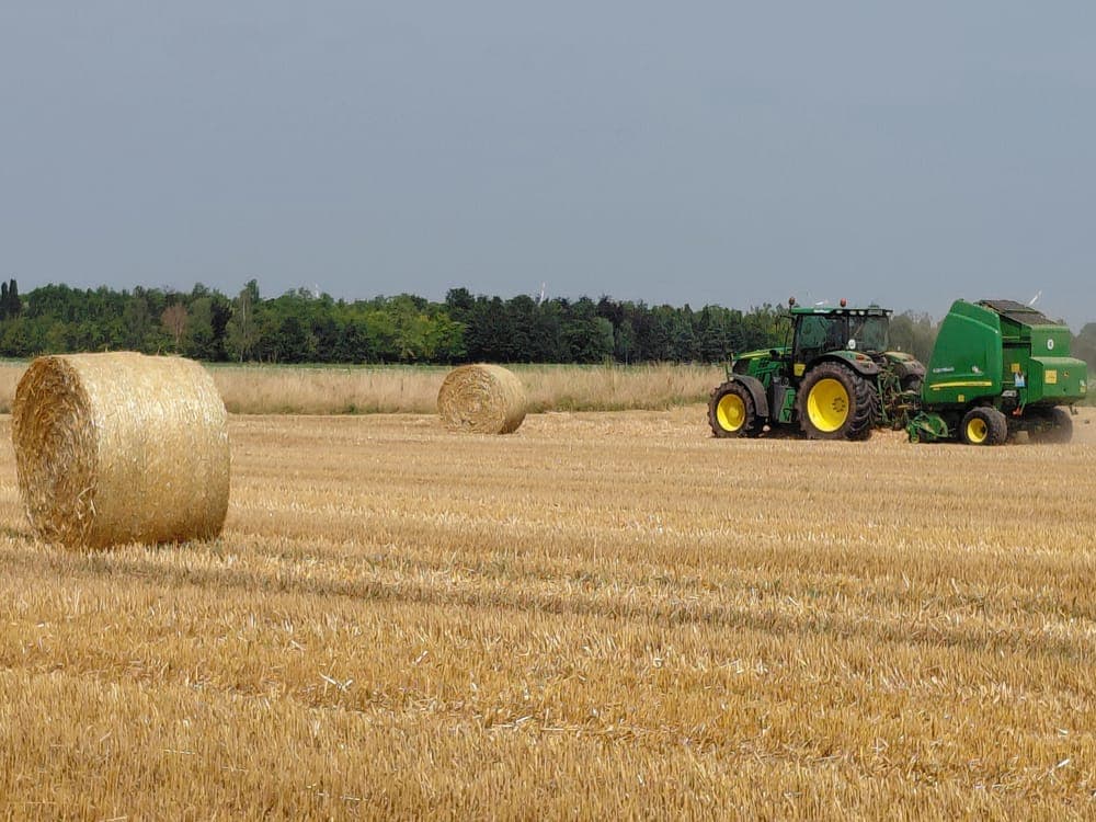 A green tractor baling straw in a field
