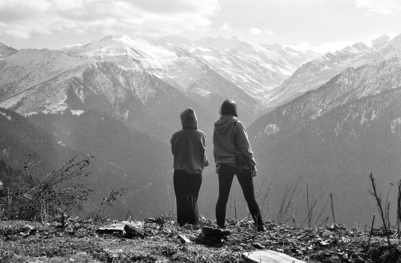 Two people looking out over a wide mountain valley from a rocky ridge