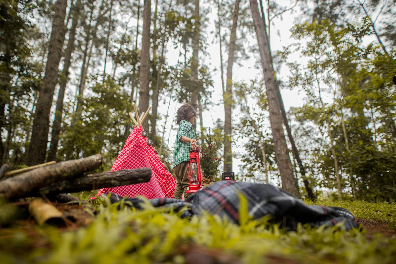 A young child at a forest campsite with a tent and a lantern